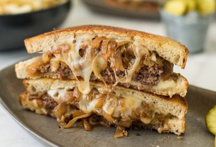 A patty melt cut in half and stacked on top of each other to show melted cheese and onions