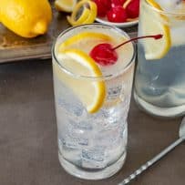 A tall glass filled with ice and Tom Collins garnished with lemon slices and a cherry