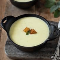Cornbread, sage and onion soup in a black bowl garnished with cornbread croutons and a crispy sage leaf