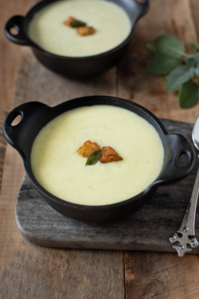 Cornbread, sage and onion soup in a black bowl garnished with cornbread croutons and a crispy sage leaf