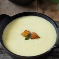 A lovely, pale green hue of the soup against a black cast iron bowl with crispy cornbread croutons on top