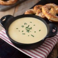 A black cast iron soup bowl filled with beer cheese soup, garnished with chopped chives and served with soft pretzels