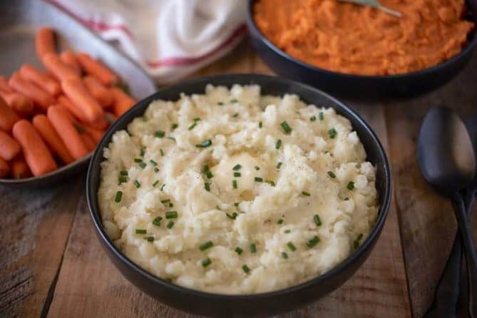 Creamy microwave mashed potatoes in a black bowl topped with chives, carrots and mashed sweet potato