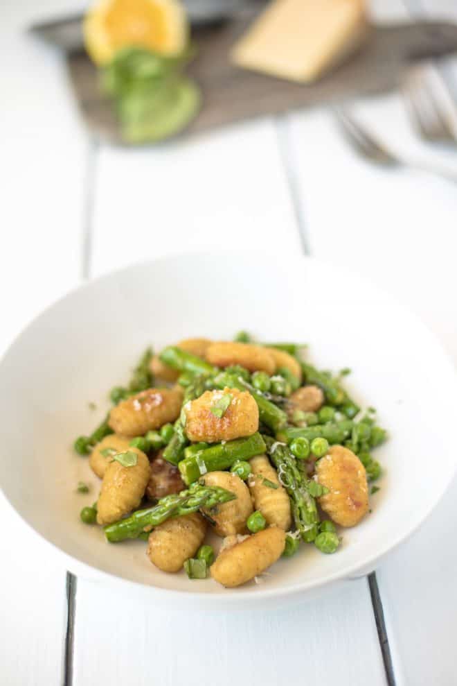A white bowl filled with crispy gnocchi mixed with fresh asparagus and peas