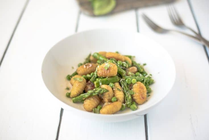 Green asparagus and peas with crispy gnocchi in a white bowl