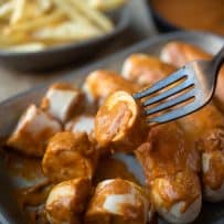 A slice of sausage and currywurst sauce on a fork