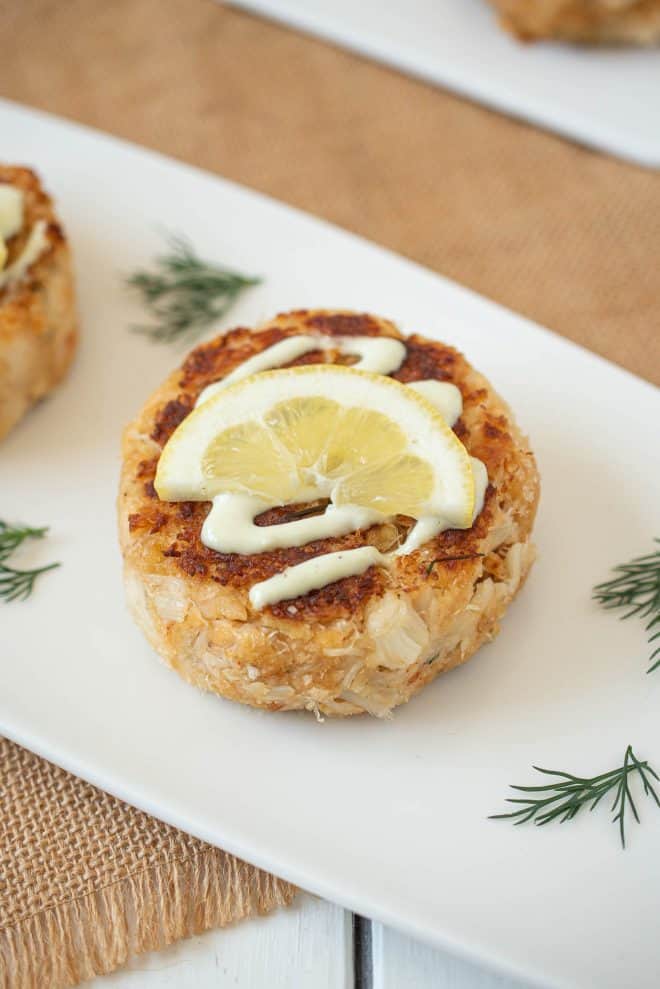 A Dungeness crab cake on a plate with sauce, lemon and dill