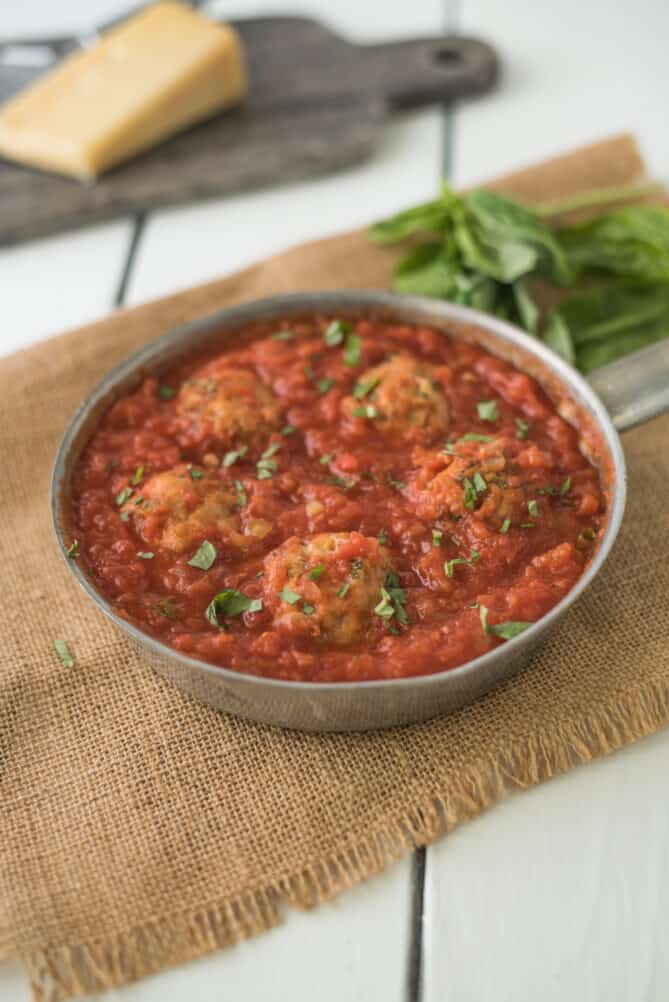 5 chicken meatballs in a shallow pan with fresh basil