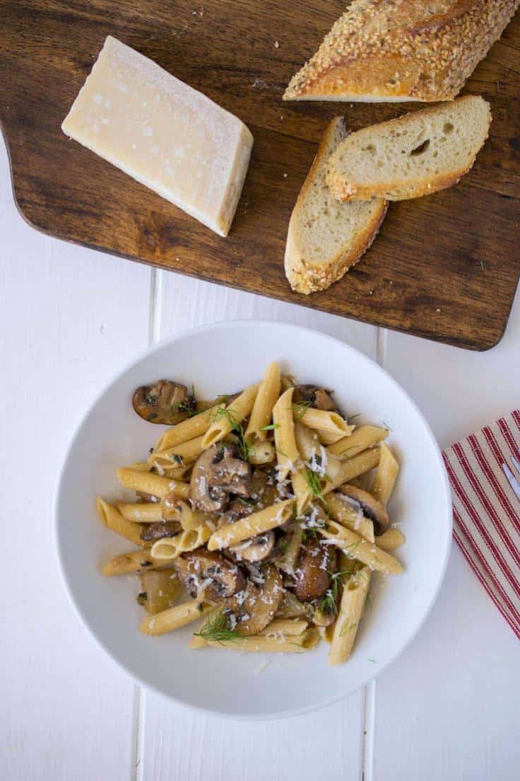 An overhead image of the pasta in a white bowl with a napkin, bread and cheese