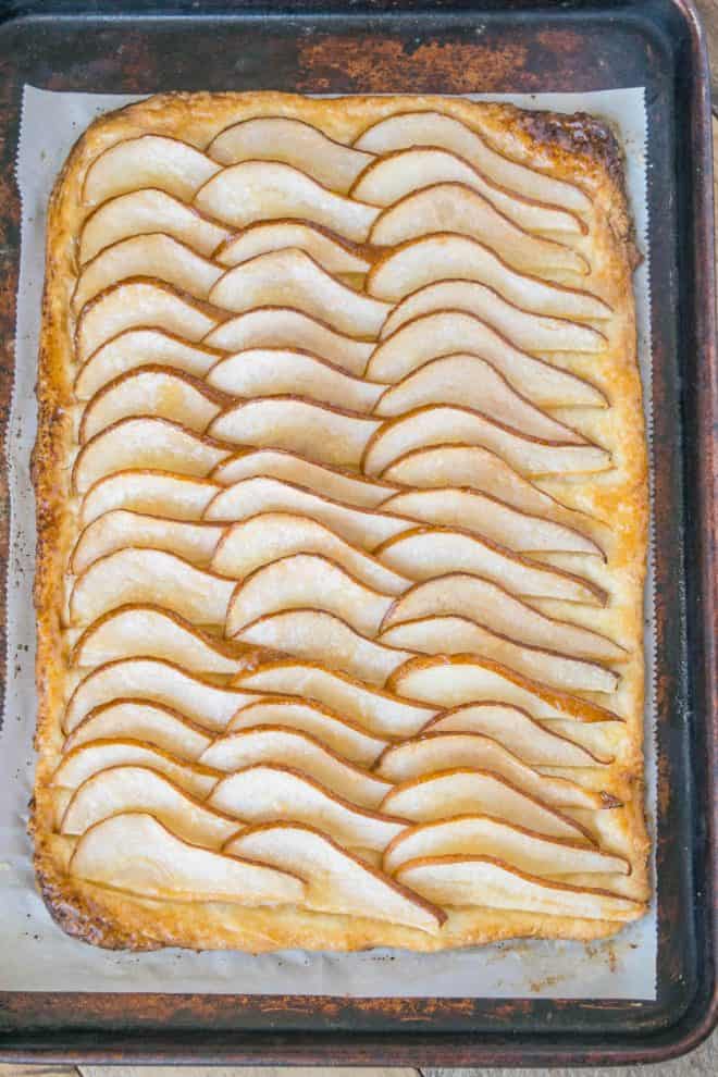 A whole pear tart on a baking sheet with the pear slices in a fan design