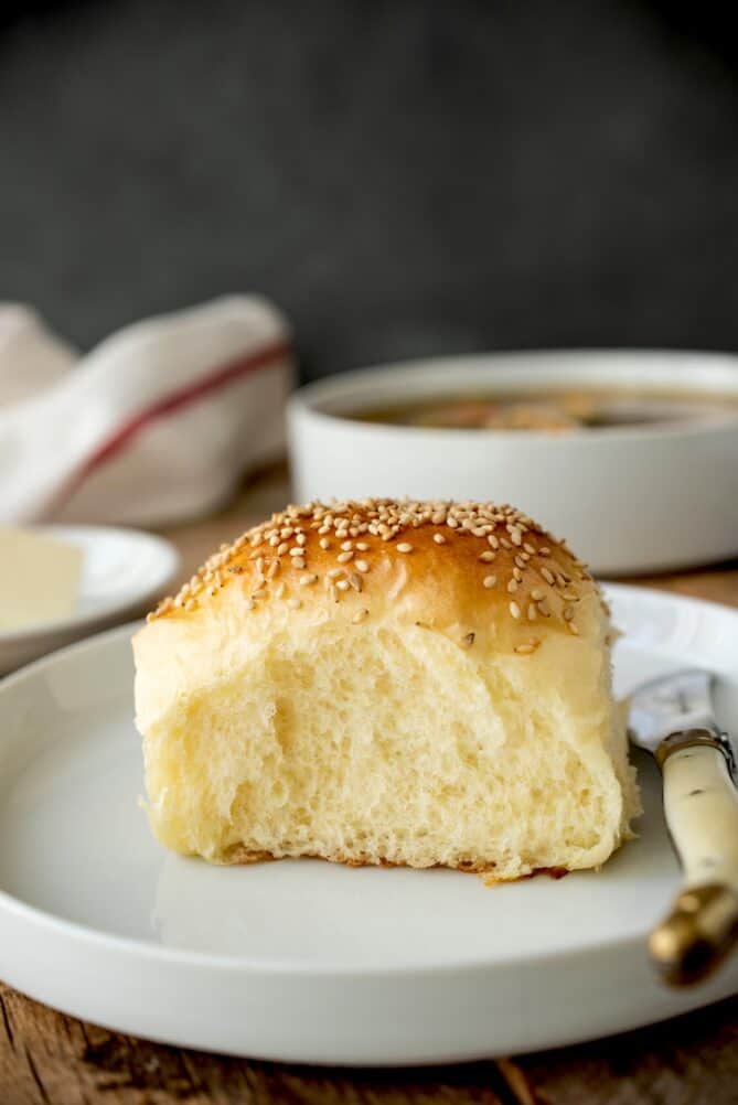 A single bread roll on a white plate with a knife