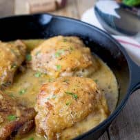 A cast iron skillet cooking up 4 chicken thighs in a Dijon sauce