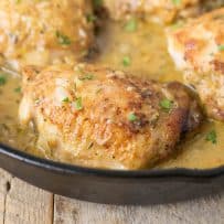 A closeup of a browned chicken thigh in a cast iron pan bathed in Dijon sauce