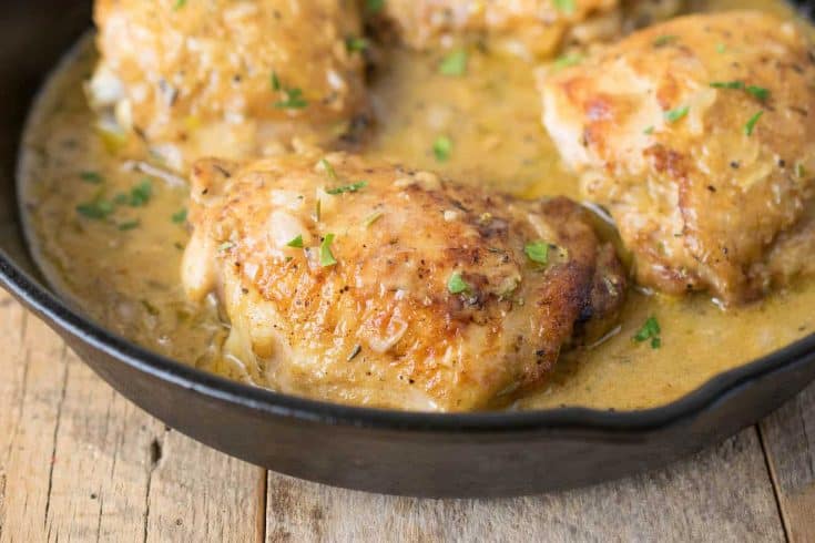 A closeup of a browned chicken thigh in a cast iron pan bathed in Dijon sauce