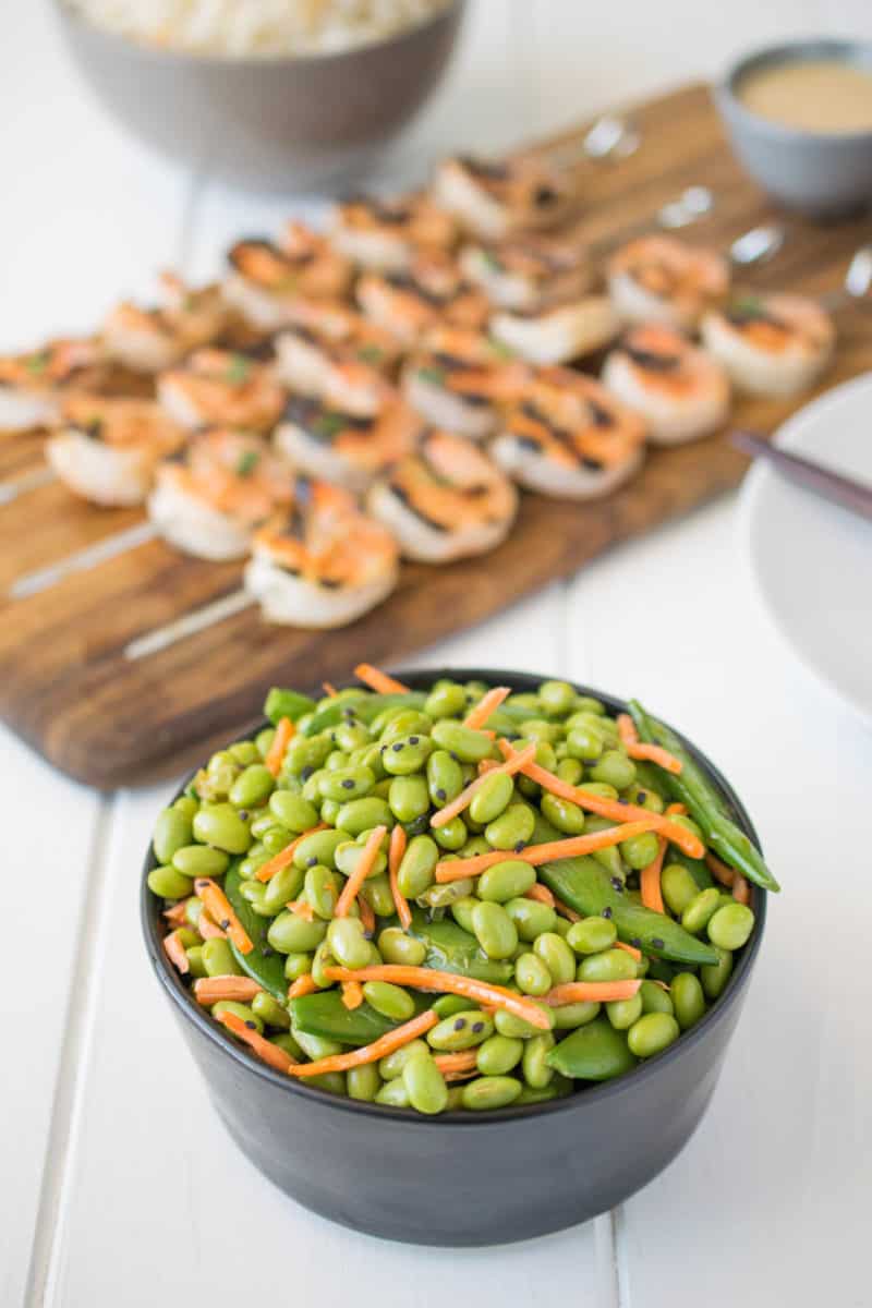 Edamame and snap peas in a black bowl with grilled shrimp