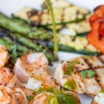 A plate of grilled shrimp and vegetables being drizzled with herb sauce
