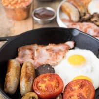 Sausages, tomato, mushrooms, bacon and egg in a cast iron skillet