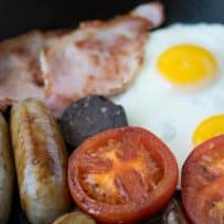 A closeup of a browned tomato with mushrooms, sausage, bacon and eggs