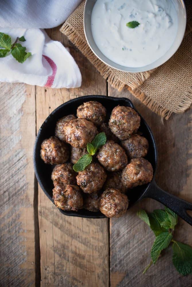 An overhead view of Greek meatballs in a cast iron skillet with Greek yogurt sauce