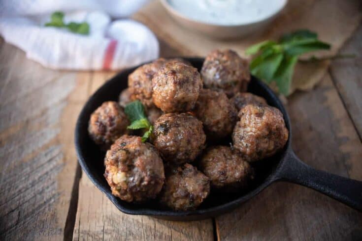 A black skillet full of browned meatballs
