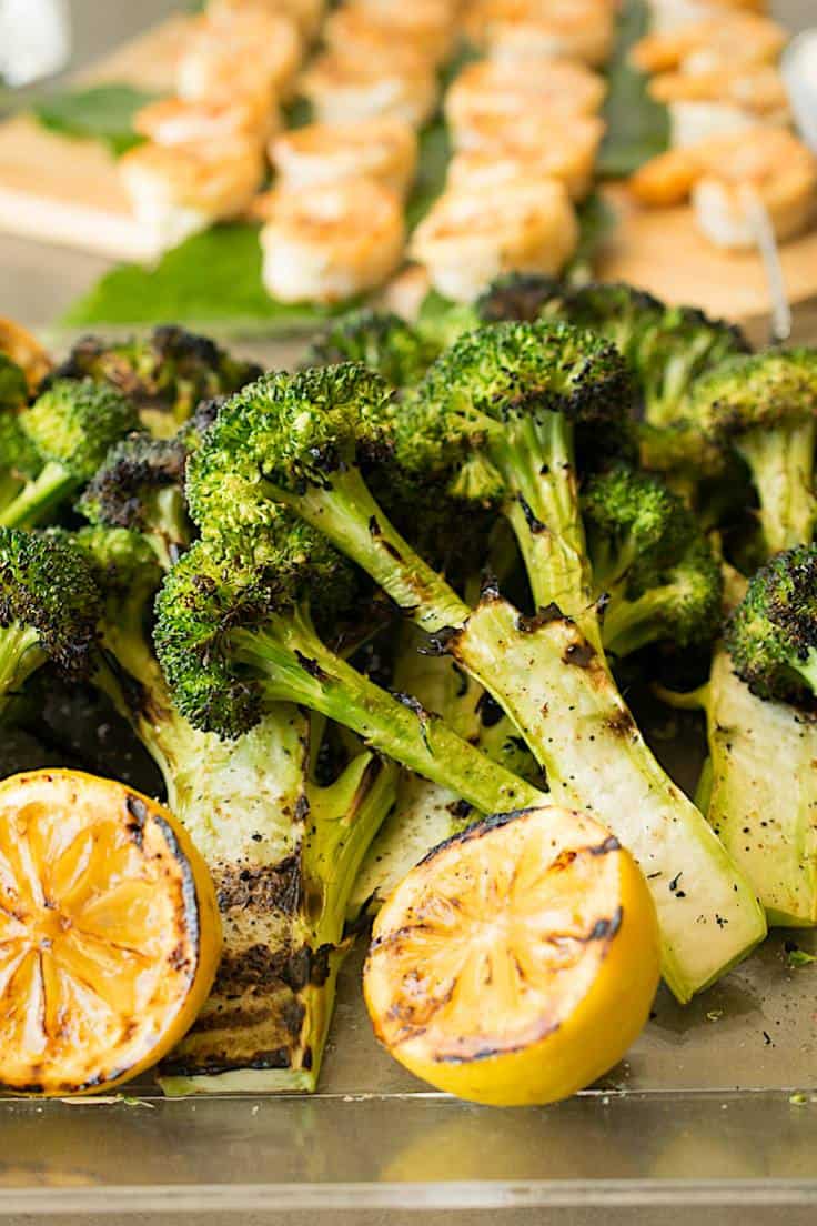 A tray of grilled broccoli with lemon and shrimp