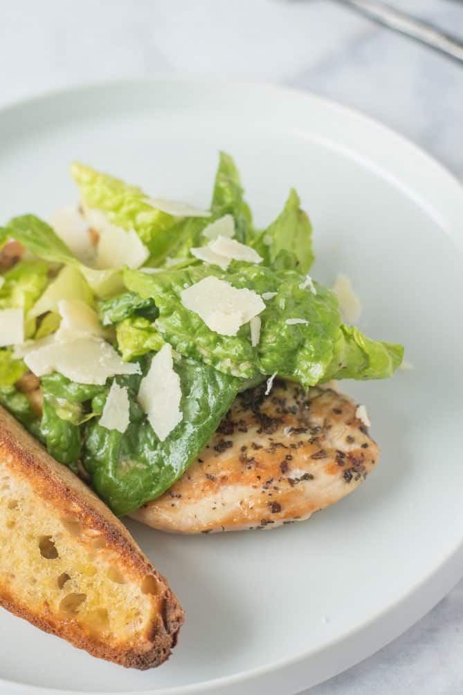Shaved Parmesan on top of lettuce with a whole chicken breast and crusty bread