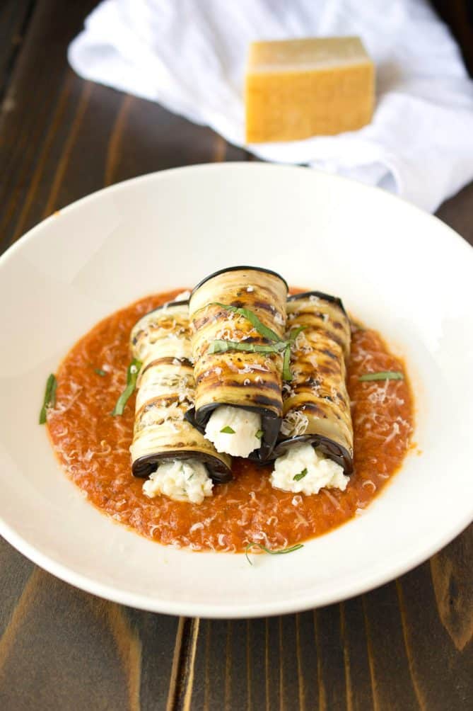 3 eggplant rollatini with ricotta cheese oozing out from the edges with marinara sauce and basil