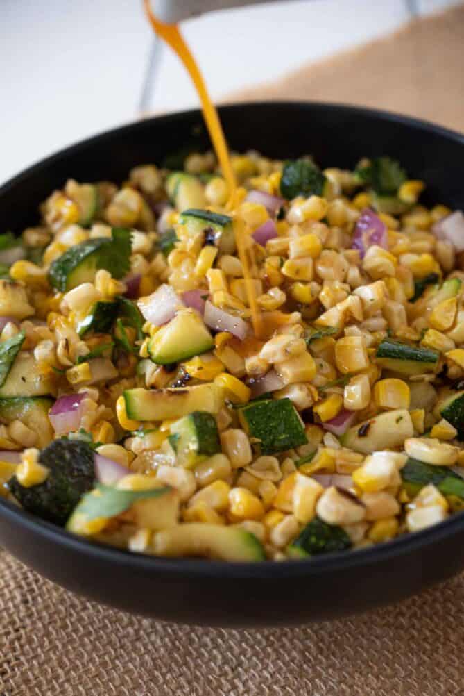 Pouring a jalapeno dressing onto grilled corn and squash salad