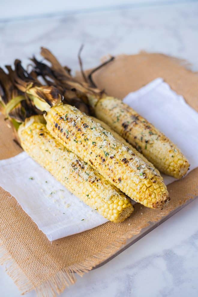 Grilled corn cobs coated with butter, garlic, Parmesan cheese and basil