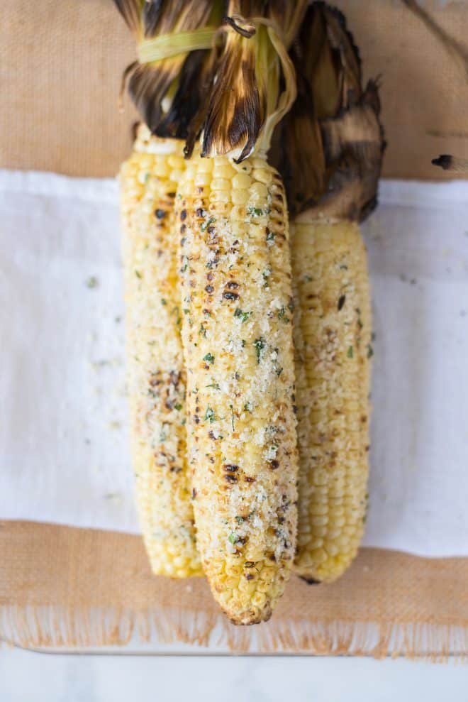 3 corn cobs that are grilled and covered with cheese, garlic and herbs