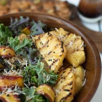 A wood bowl of green and red kale topped with grilled pineapple, shaved carrots and toasted coconut