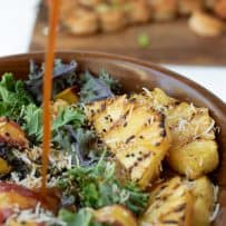 Pineapple with grill marks in a kale salad with salad dressing being poured