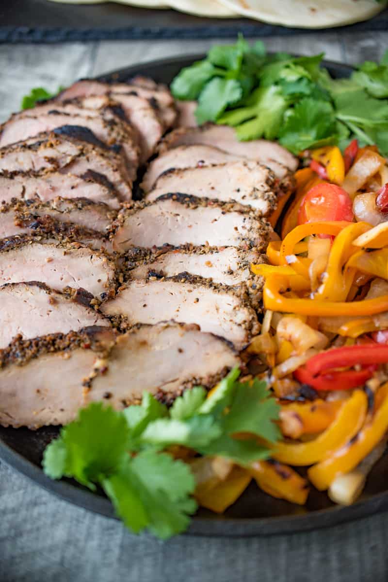 Grilled pork tenderloin fajitas are a quick and easy way to get a summer meal served in under 30 minutes. Marinated pork tenderloin is grilled along with onions and peppers. The pork is sliced then all are served on warm tortillas garnished with fresh avocado and cilantro.