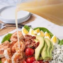 Pouring salad dressing over a grilled shrimp cobb salad