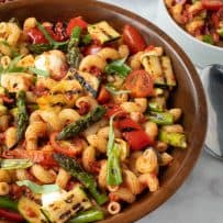 Colorful grilled vegetables in a wood bowl of pasta mixed with sun-dried tomato pesto