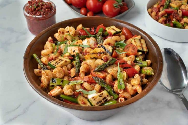 A large wood bowl filled with grilled vegetable sun-dried tomato pesto pasta with asparagus, red peppers, zucchini, spring onions and tomatoes