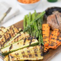 Grilled zucchini, carrots, asparagus and mushrooms on a serving board with sun-dried tomato dip