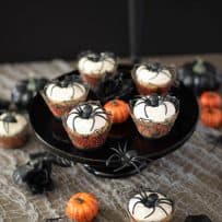 5 spider cupcakes on a black cake stand with some cupcakes underneath