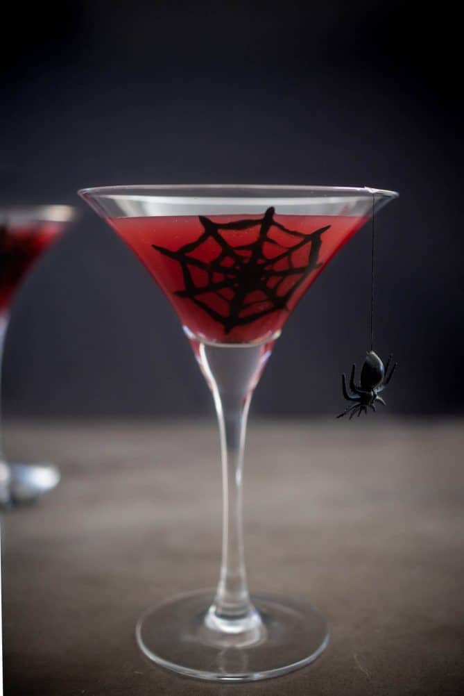 A spooky Halloween drink of a blood orange martini with a spider web and spider on the glass