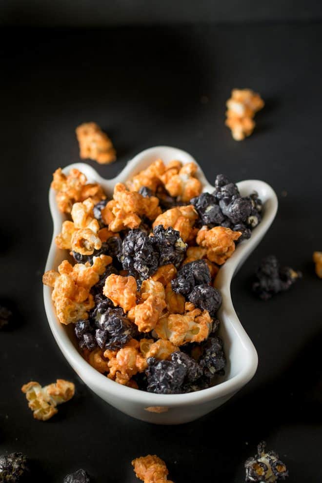A white bowl in the shape of a ghost filled with orange and black popped corn