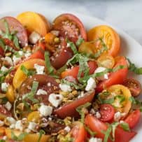 A colorful display of large and small tomatoes that are sliced and served with feta cheese, pistachios and basil