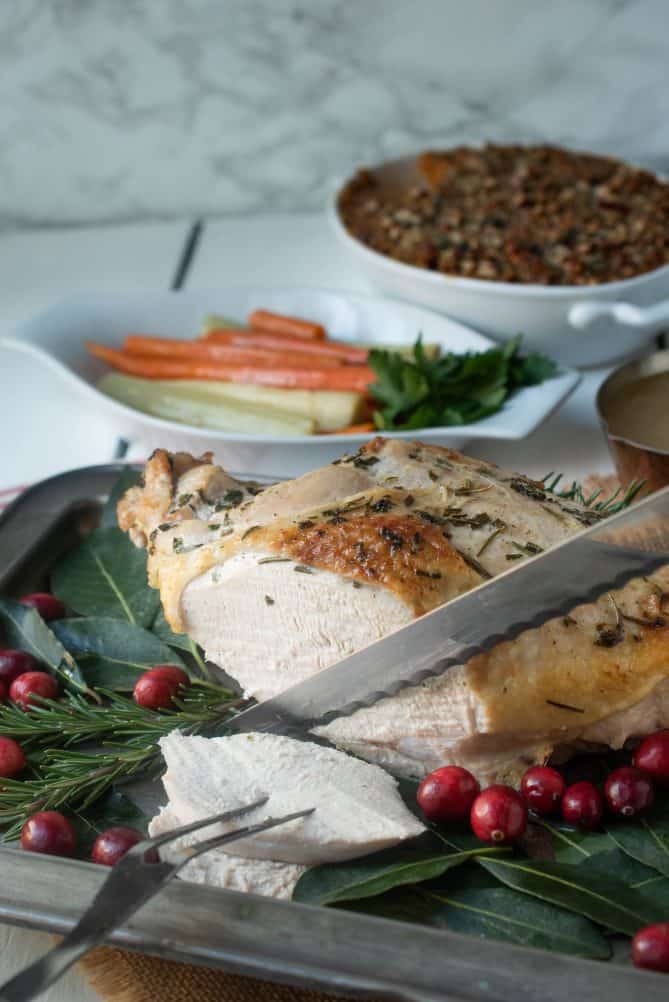 Carving slices of a roast turkey breast with carrots in the background and a sweet potato casserole