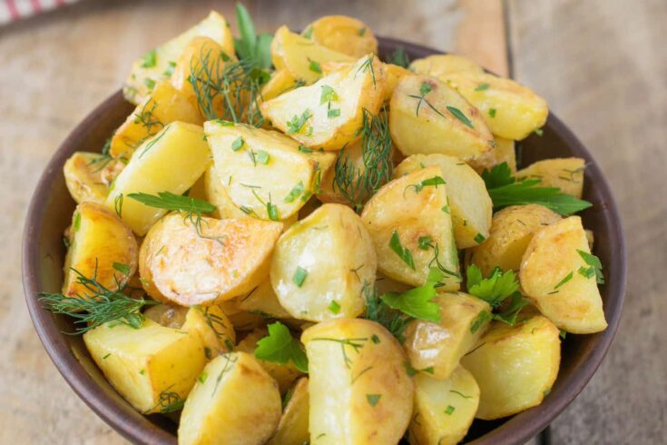 A closeup of potato wedges in potato salad with fresh herbs