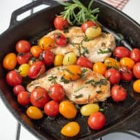 A cast iron skillet with 2 chicken breast, tomatoes and herbed butter