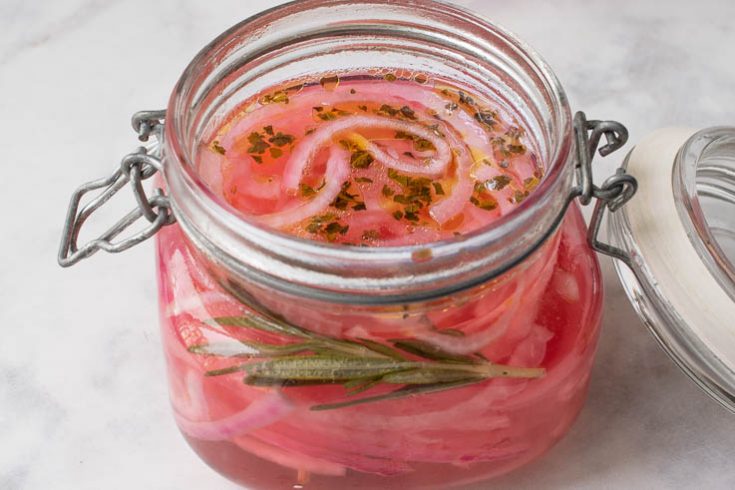 A sealable jar with red onions pickling in vinegar and herbs