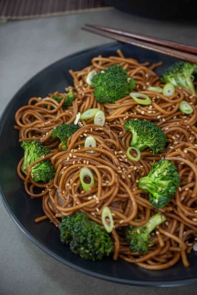 A black plate with hoisin coated noodles with broccoli