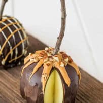A chocolate apple drizzled with peanut butter and pecans on a wood plank