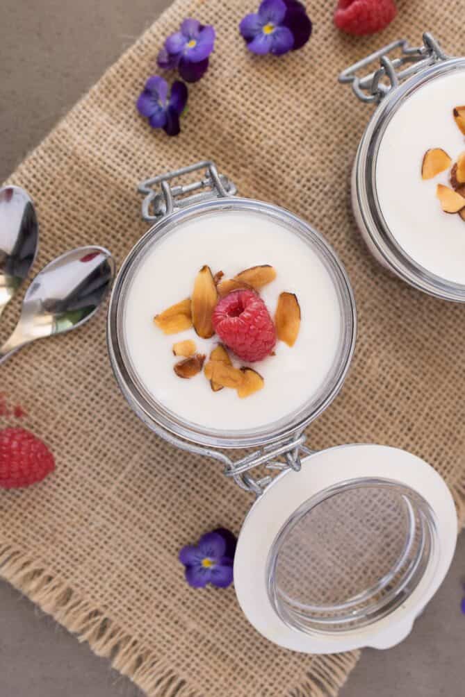 A jar of yogurt topped with nuts and a raspberry view from overhead
