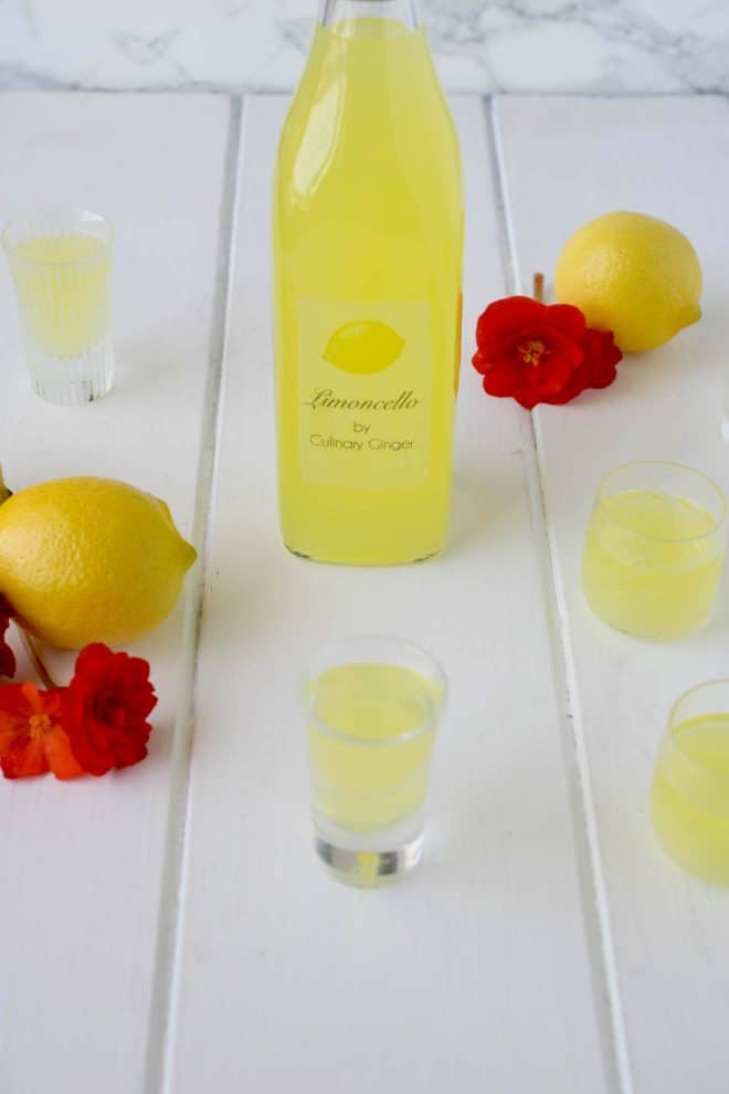A bottle of limoncello with glasses, lemons and red flowers