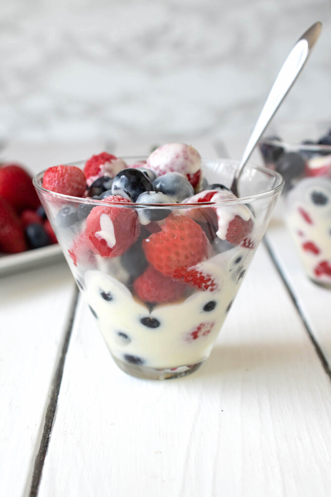 A side view of a glass bowl with fruit and custard